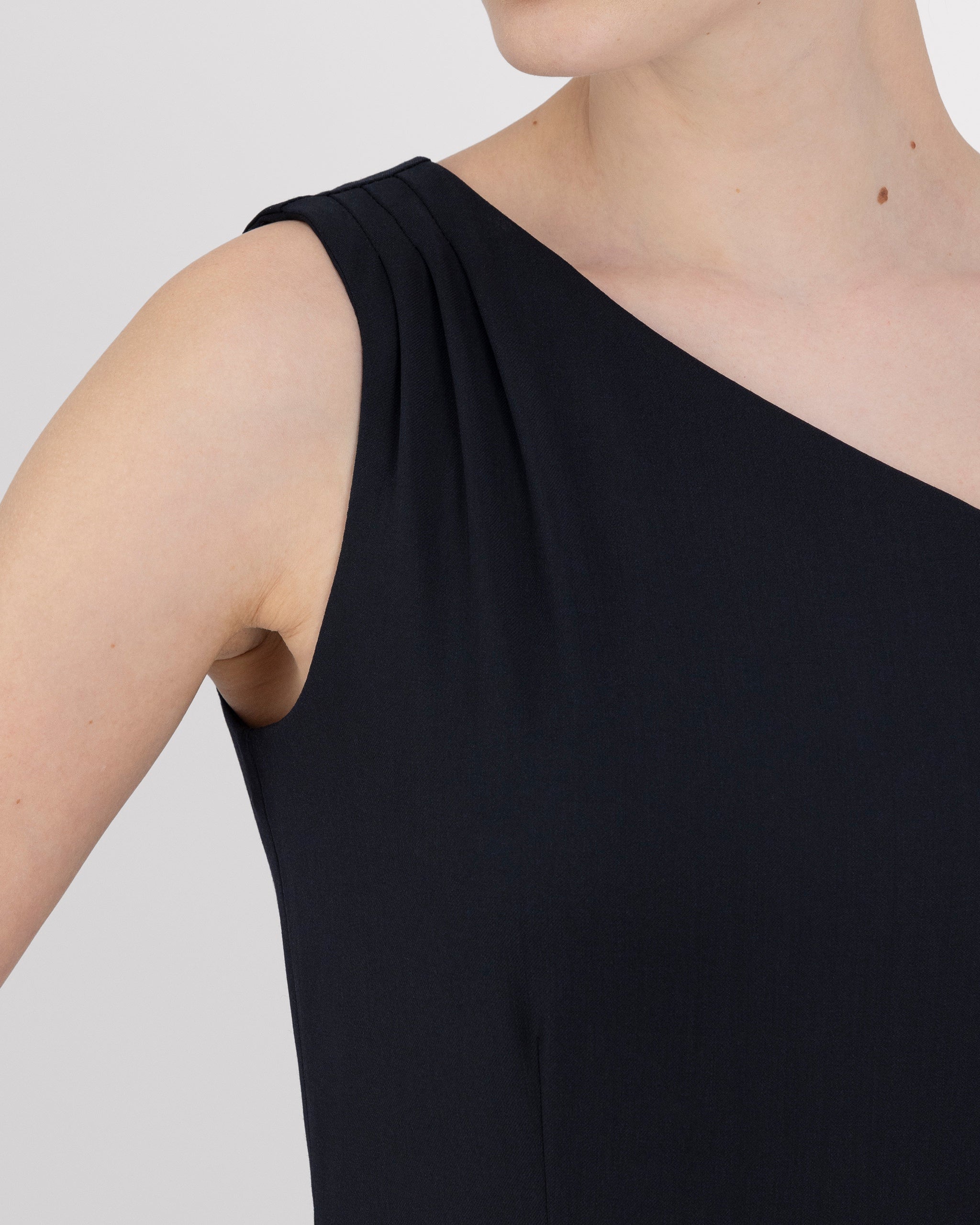 Asymmetrisches Kleid mit einer Schulter und feinen Falten für eine elegante Drapierung. Figurbetonte Silhouette mit präzisen Abnähern, knielangem Schnitt und rückwärtigem Gehschlitz. Unsichtbarer Reissverschluss an der Seite und feiner Blindsaum für ein modernes, minimalistisches Design.