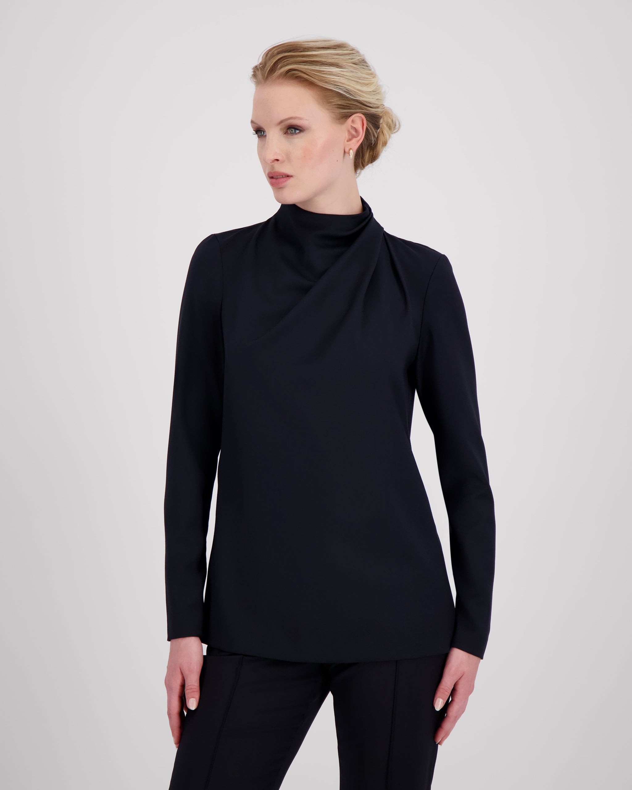 Top mit hochgeschlossenem, sanft drapiertem Stehkragen und feinem Rückenschlitz mit drei goldenen Knöpfen als dezentes, edles Detail. Zweifach umgeschlagene Ärmel und ein schmal abgesteppt Saum betonen die präzise Linienführung. Die körpernahe, weich fliessende Passform verbindet skulpturale Eleganz mit femininer Leichtigkeit.