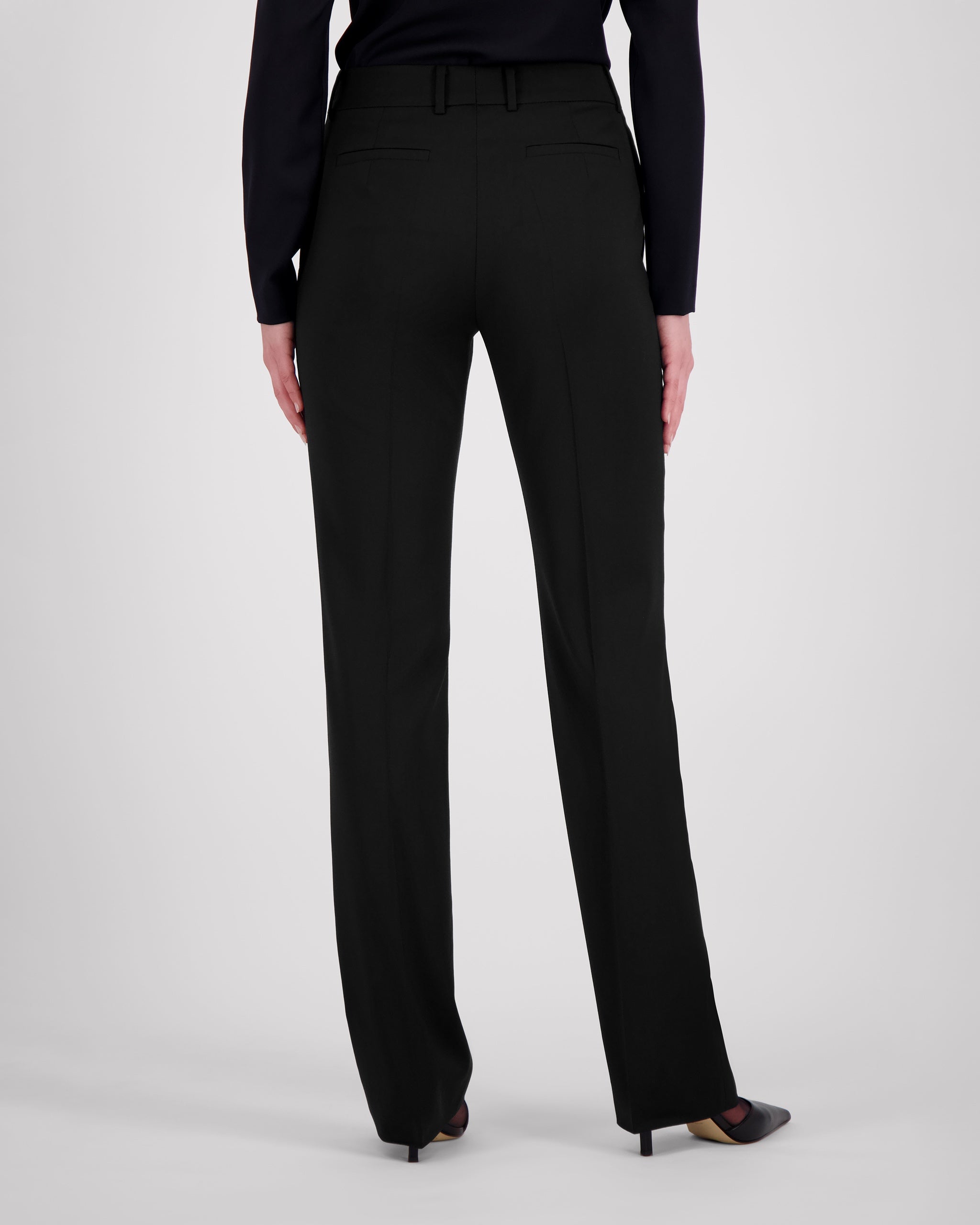 Elegante Hose aus schwarzer Merinowolle mit schmaler Passform und fliessendem Fall. Charakteristische Mittelnaht vorn, dezente Bügelfalte hinten. Verdeckter Bundverschluss mit Corozo-Knopf für eine glatte Frontpartie. Seitliche Eingrifftaschen, rückwärtige Pattentaschen und feine Abnäher formen eine feminine Silhouette mit klarer Linienführung.
