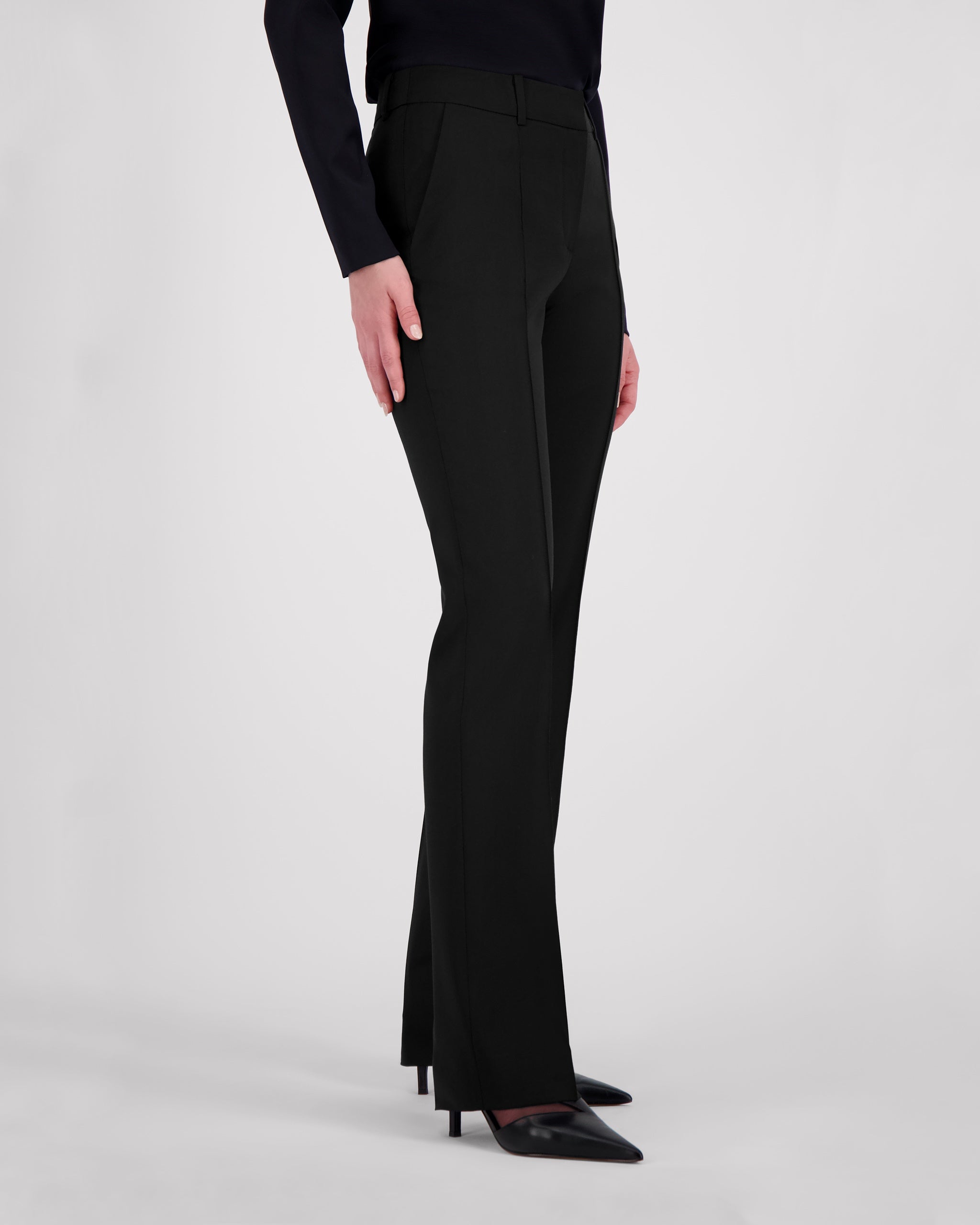 Elegante Hose aus schwarzer Merinowolle mit schmaler Passform und fliessendem Fall. Charakteristische Mittelnaht vorn, dezente Bügelfalte hinten. Verdeckter Bundverschluss mit Corozo-Knopf für eine glatte Frontpartie. Seitliche Eingrifftaschen, rückwärtige Pattentaschen und feine Abnäher formen eine feminine Silhouette mit klarer Linienführung.