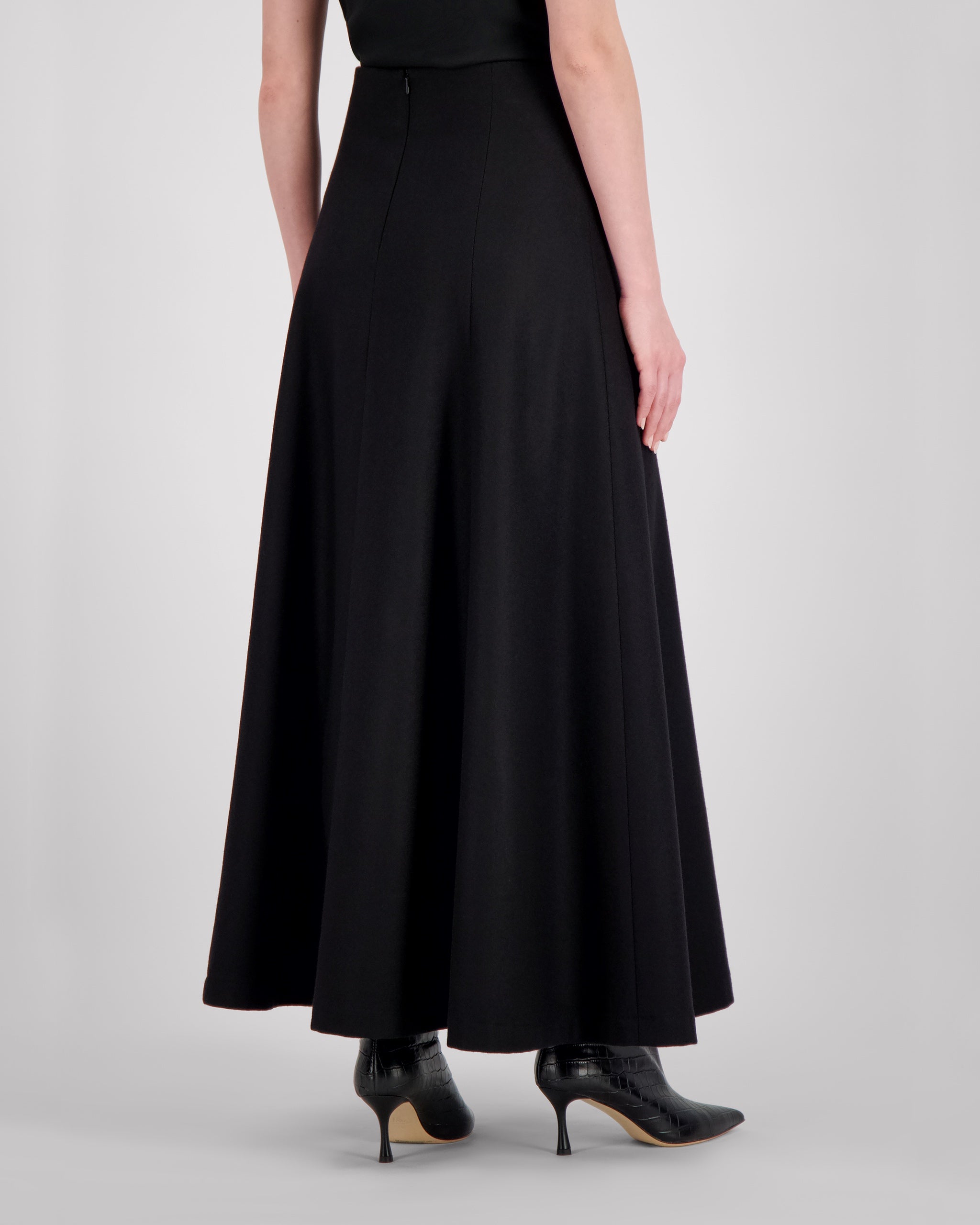 Knöchellanger Rock aus reiner schwarzer Merinowolle mit klarer, weich fallender Silhouette. Ungesteppt gearbeitete Silhouettennähte sorgen für skulpturale Eleganz. Der nahtverdeckte Reissverschluss hinten und der doppelt umgeschlagene, fein abgesteppt Saum vollenden die Form mit technischer Präzision und stabiler Linienführung.
