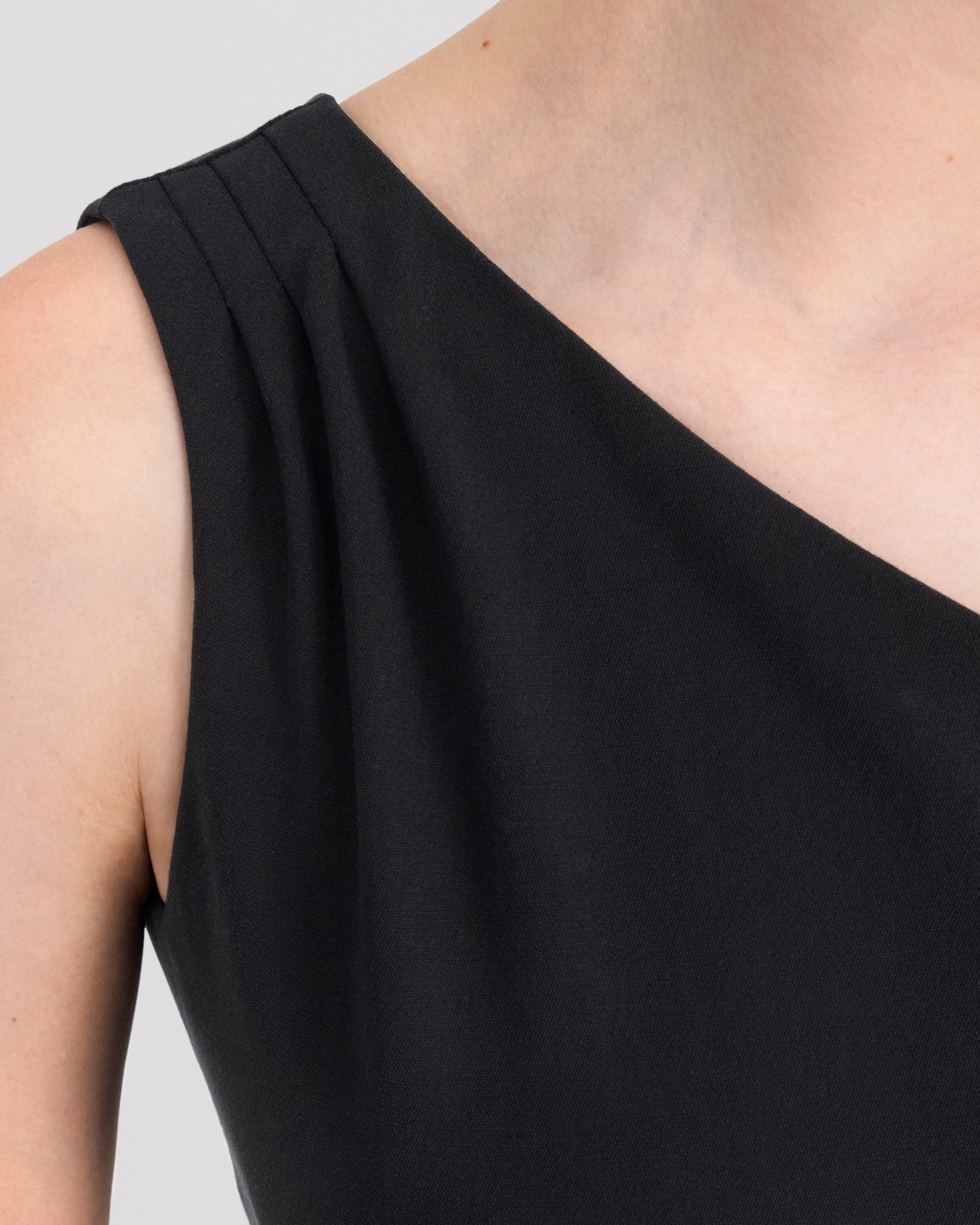 Asymmetrisches Kleid mit skulpturaler Schulterlinie und drei feinen Falten für eine fliessende Drapierung. Figurformende Abnäher vorn und hinten betonen eine elegante Silhouette. Unter dem Knie endend, mit rückwärtigem Gehschlitz für Bewegungsfreiheit. Nahtverdeckter Reissverschluss an der Seite und Blindsaum für ein puristisches Finish.