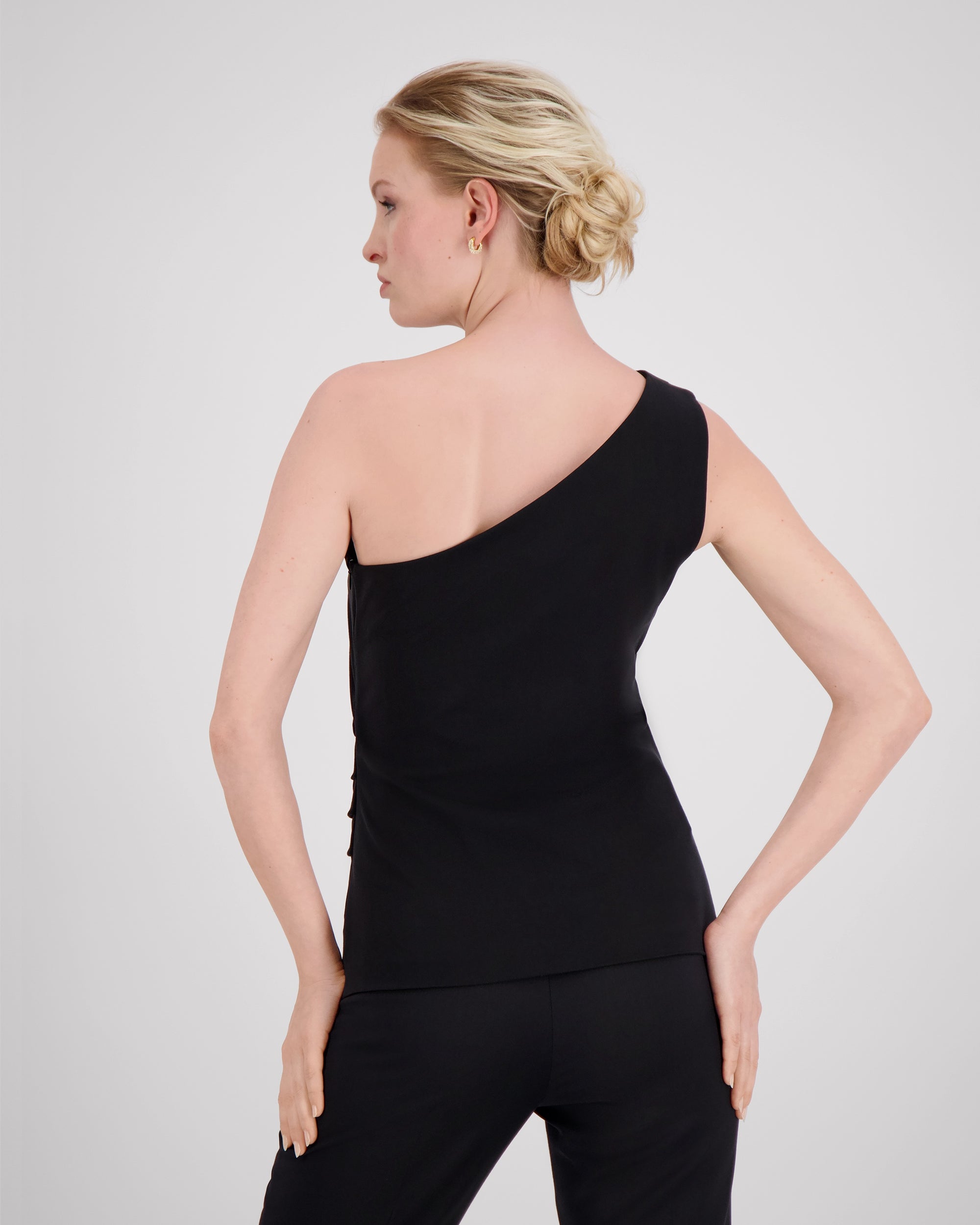 Top mit charakteristischer Schulterfalte und sanft drapierter Seitennaht für eine skulpturale, dynamische Silhouette. Körpernaher Schnitt mit feinem Contouring betont die Figur weich und kraftvoll. Verdeckter Reissverschluss an der linken Seite und Blindsaum am geraden Hüftabschluss unterstreichen das puristische, fliessende Design.