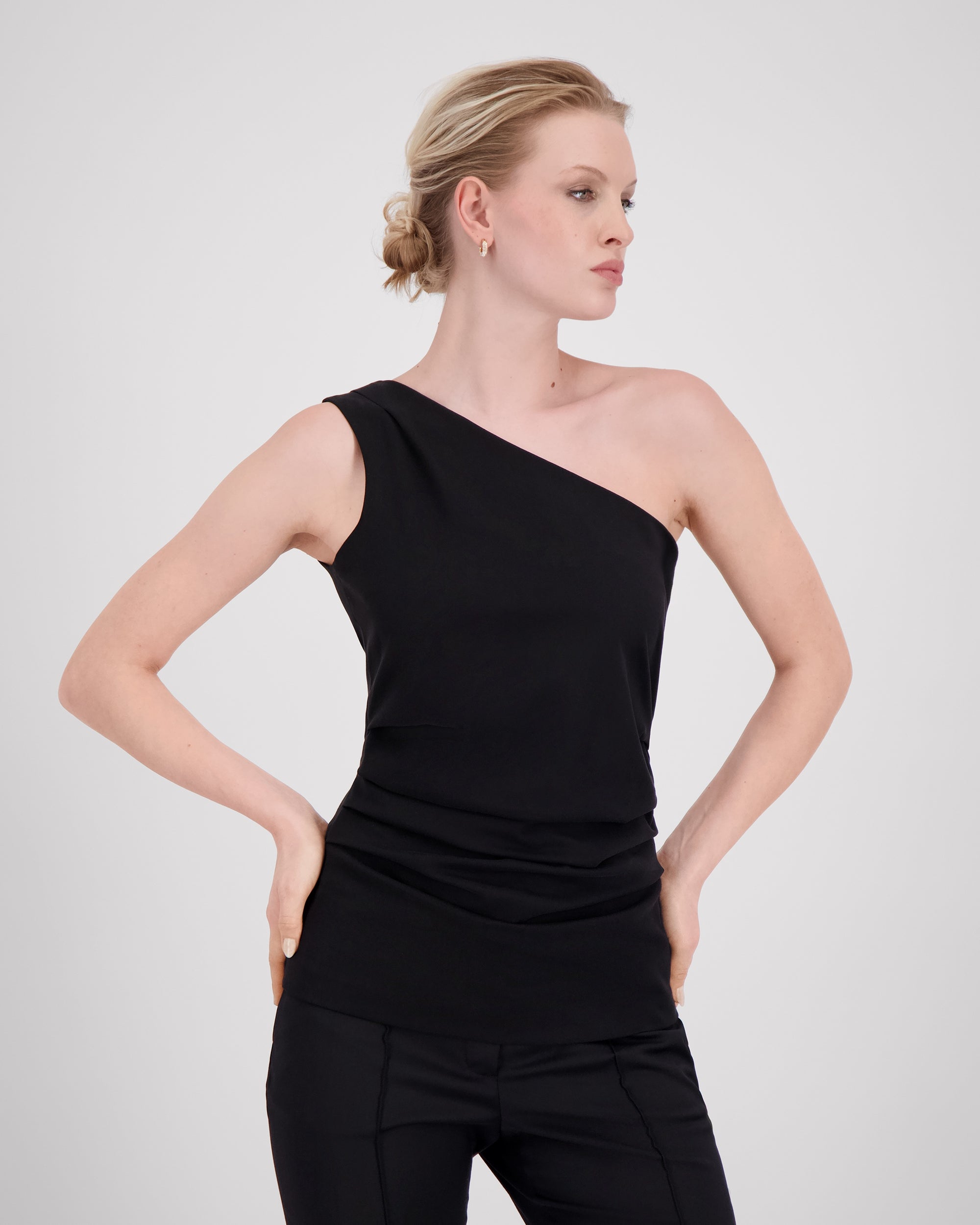 Top mit charakteristischer Schulterfalte und sanft drapierter Seitennaht für eine skulpturale, dynamische Silhouette. Körpernaher Schnitt mit feinem Contouring betont die Figur weich und kraftvoll. Verdeckter Reissverschluss an der linken Seite und Blindsaum am geraden Hüftabschluss unterstreichen das puristische, fliessende Design.