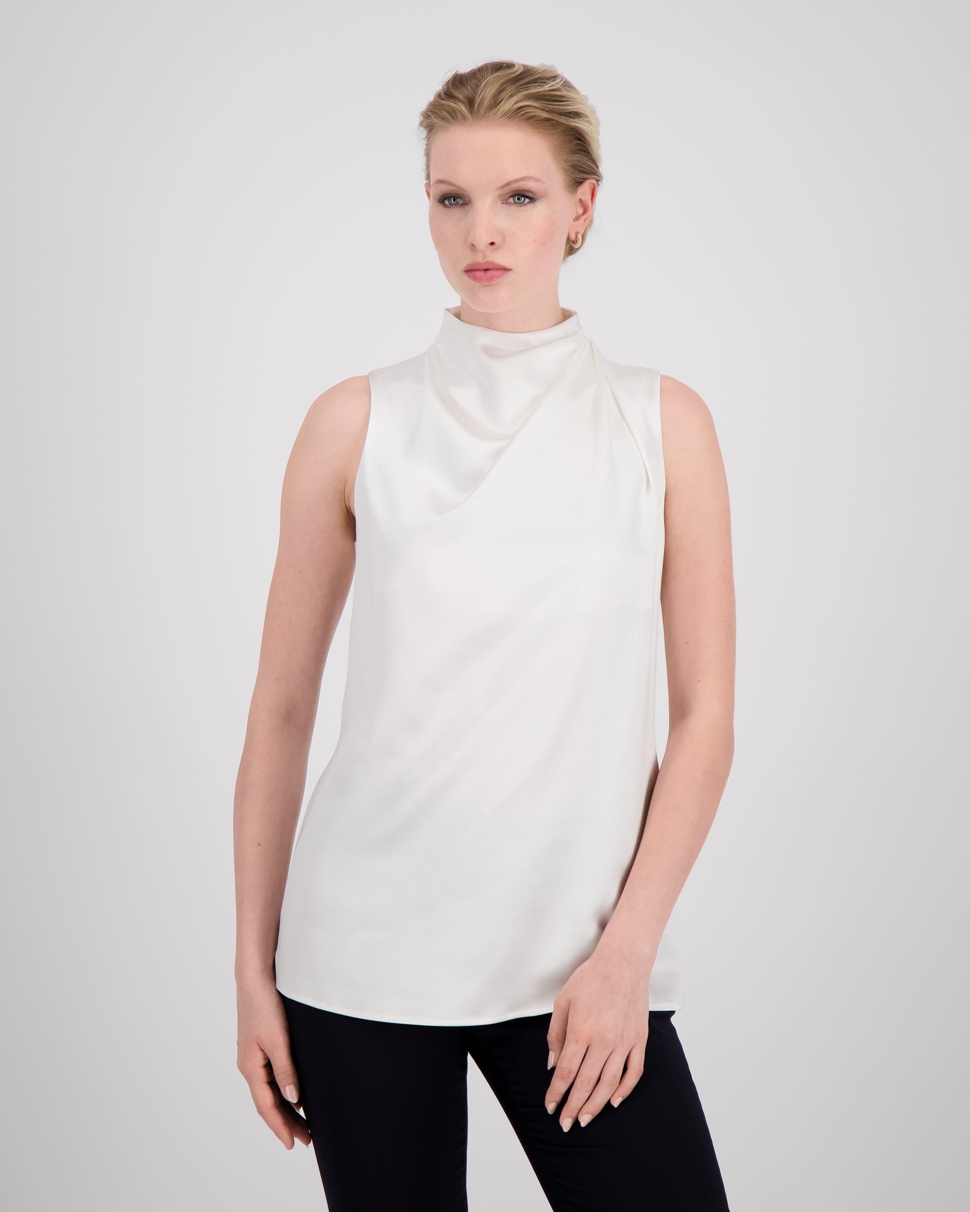 Asymmetrisch geschnittenes Top mit sanft drapierter Schulter für eine feminine, schwungvolle Silhouette. Der hochgeschlossene Stehkragen wird im Rückenteil durch einen feinen Schlitz und drei goldene Knöpfe mit filigranen Knopfschlingen akzentuiert. Ein edles Detail, das das puristische Design um eine subtile Note von Noblesse ergänzt.