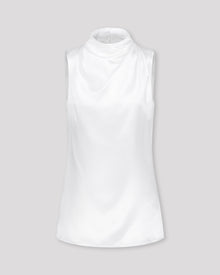 Asymmetrisch geschnittenes Top mit sanft drapierter Schulter für eine feminine, schwungvolle Silhouette. Der hochgeschlossene Stehkragen wird im Rückenteil durch einen feinen Schlitz und drei goldene Knöpfe mit filigranen Knopfschlingen akzentuiert. Ein edles Detail, das das puristische Design um eine subtile Note von Noblesse ergänzt.