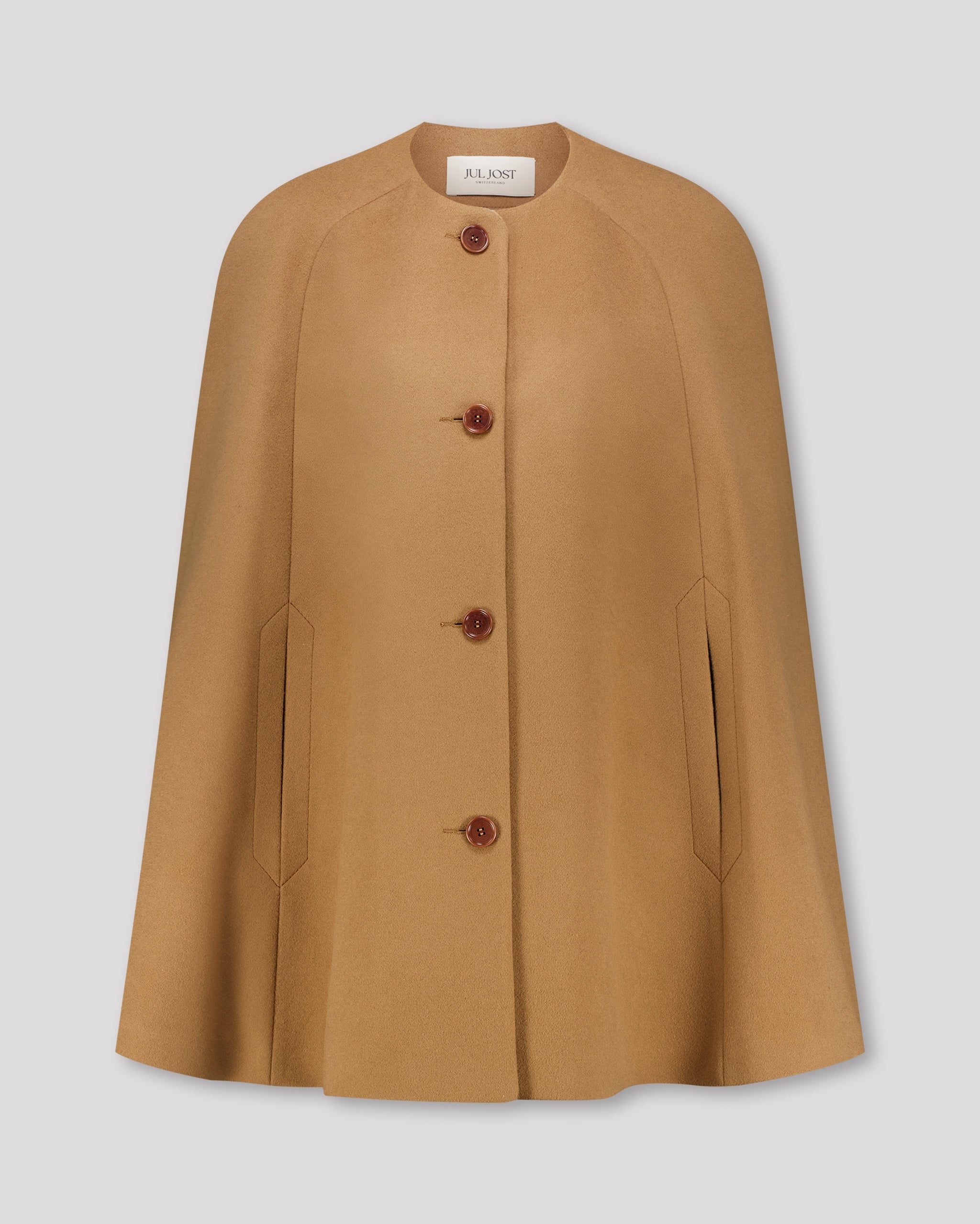 Cape-Mantel aus reinem Kaschmir mit sanft modellierenden Schulterabnähern und fein gearbeiteten Ärmelschlitzen mit zarter Absteppung. Der matte Vier-Knopf-Verschluss aus Corozo hält die Silhouette klar und puristisch. Dezente Eingriffschlitze und eine versteckte Innentasche verbinden Funktionalität mit eleganter, reduzierter Formensprache.