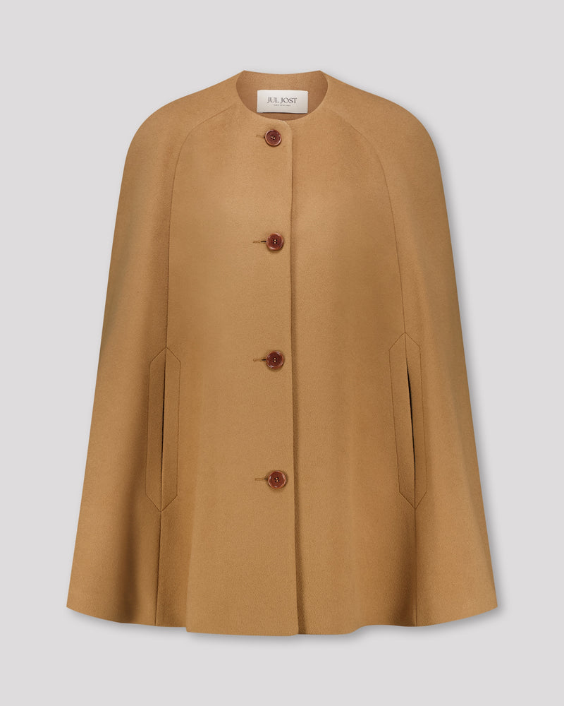 Cape-Mantel aus reinem Kaschmir mit sanft modellierenden Schulterabnähern und fein gearbeiteten Ärmelschlitzen mit zarter Absteppung. Der matte Vier-Knopf-Verschluss aus Corozo hält die Silhouette klar und puristisch. Dezente Eingriffschlitze und eine versteckte Innentasche verbinden Funktionalität mit eleganter, reduzierter Formensprache.