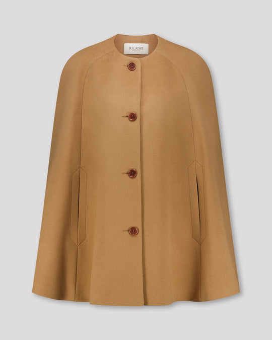 Cape-Mantel aus reinem Kaschmir mit sanft modellierenden Schulterabnähern und fein gearbeiteten Ärmelschlitzen mit zarter Absteppung. Der matte Vier-Knopf-Verschluss aus Corozo hält die Silhouette klar und puristisch. Dezente Eingriffschlitze und eine versteckte Innentasche verbinden Funktionalität mit eleganter, reduzierter Formensprache.