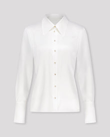 Bluse aus Peace Silk mit modernem, leicht vergrössertem Kragen und feiner Kantensteppung für einen ausdrucksstarken Look. Nach vorne versetzte Schulternähte, Rückenfalte und locker fallende Silhouette sorgen für entspannte Eleganz. Goldene Metallknöpfe, extralange Manschetten und ein fein abgesteppt Saum unterstreichen die präzise Verarbeitung.